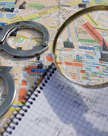 Karte einer Stadt, darau Handschellen, Notizblock und eine Lupe
