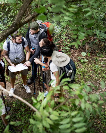 5 Personen stehen in einem Wald und orientieren sich anhand einer Karte und Kompass